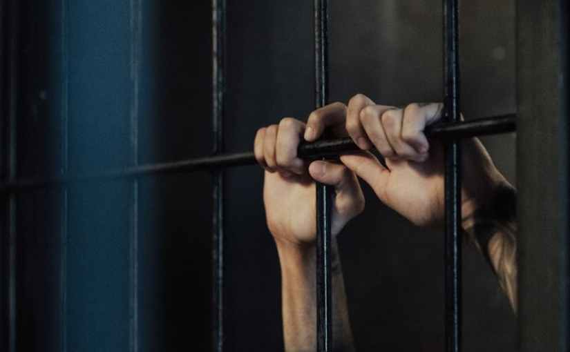 hands of a person holding on metal railings in a jail