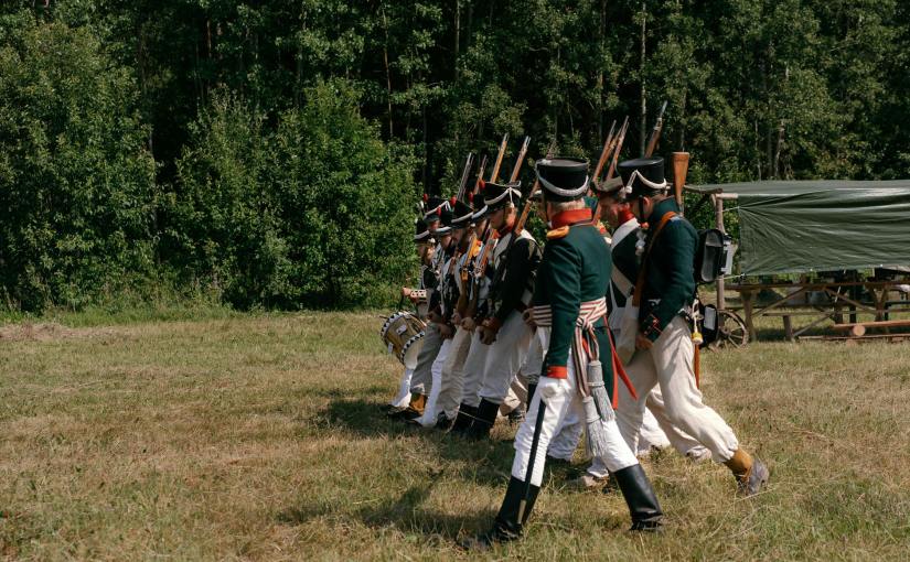 soldiers with rifles wearing historical uniforms marching in the grass field